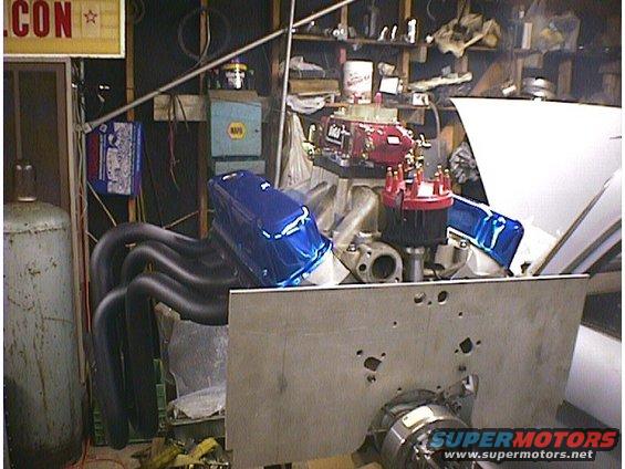 V8 engine with blue valve covers and red distributor cap, sitting in a garage