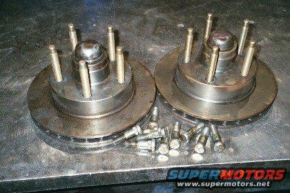 Two brake rotors with wheel studs attached, and a pile of loose wheel studs on a metal surface