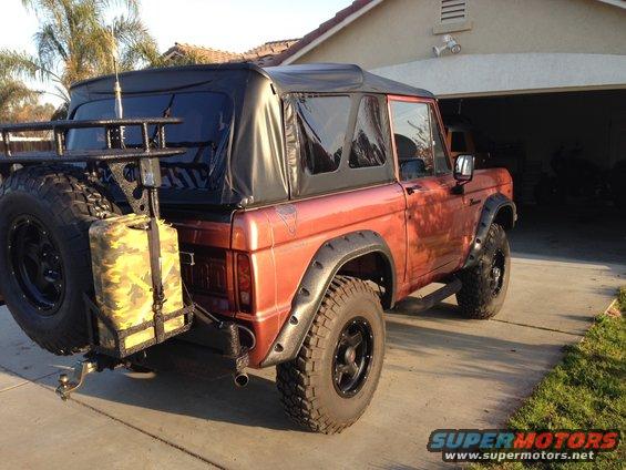 Orange Ford Bronco with soft top, spare tire carrier, and camo gas can on rear