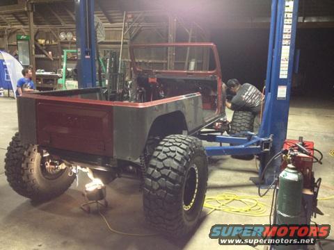 Red Jeep CJ7 body on a lift, undergoing repairs, with large off-road tires