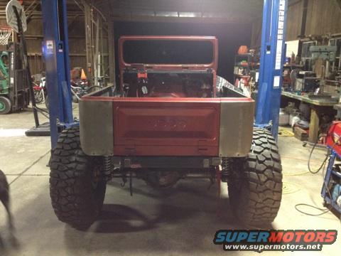 Rear view of a red Jeep CJ-series body on a lift, showing large tires and a bare interior