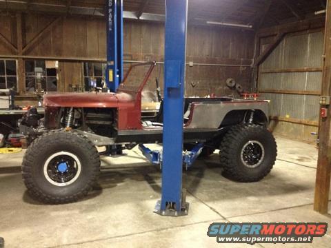 1985 Jeep CJ7 body on a custom chassis with large off-road tires, in a garage with a lift
