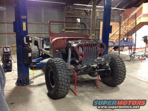 Red Jeep CJ-style vehicle on a lift, front end visible, large tires