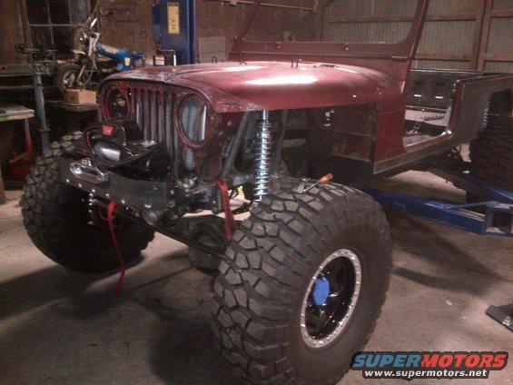 Red Jeep CJ-series body with large off-road tires and a winch, undergoing modification