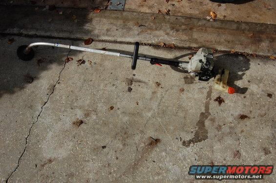 String trimmer with gas tank detached, lying on concrete