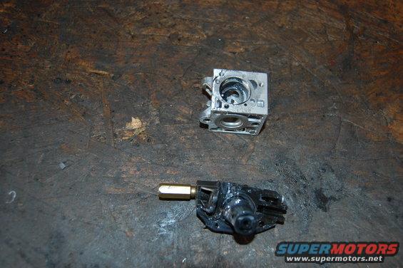 Two disassembled carburetor components on a dirty workbench surface