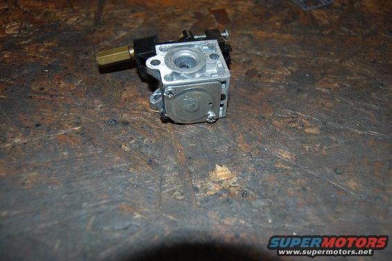 Close-up of a carburetor with a brass fitting on a wooden surface