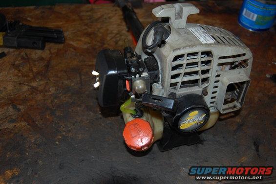 Echo weed trimmer engine with orange fuel cap and black starter housing. Grille on top is dusty