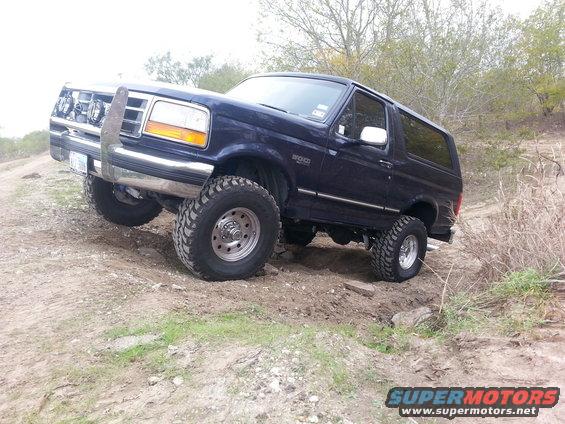 Blue 1995 Ford Bronco with aftermarket bumper and lift kit driving on a dirt trail