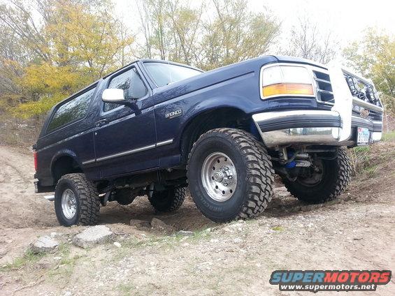 Blue 1995 Ford Bronco with lifted suspension and off-road tires on a dirt trail