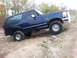 1995 Ford Bronco - A blue 1995 Ford Bronco navigates an off-road trail, demonstrating its capability on uneven terrain.