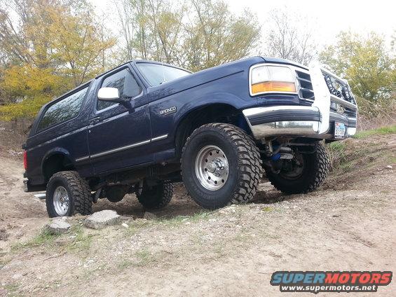 Blue 1995 Ford Bronco with off-road tires driving on a dirt path