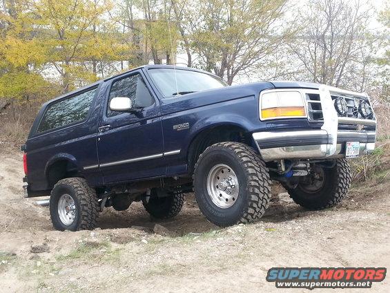 Blue Ford Bronco lifted with off-road tires, parked on dirt