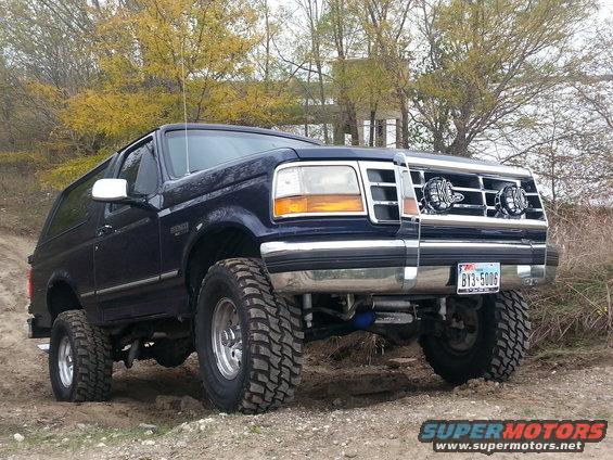 Dark blue Ford Bronco with lifted suspension and off-road tires parked on a dirt road