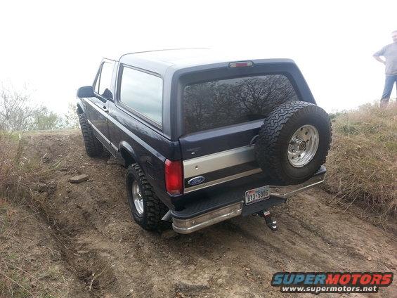 1995 Ford Bronco driving up a dirt hill with a spare tire mounted on the back