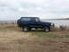 1995 Ford Bronco - A dark blue 1995 Ford Bronco is parked on a grassy bank next to a large body of water under a cloudy sky.