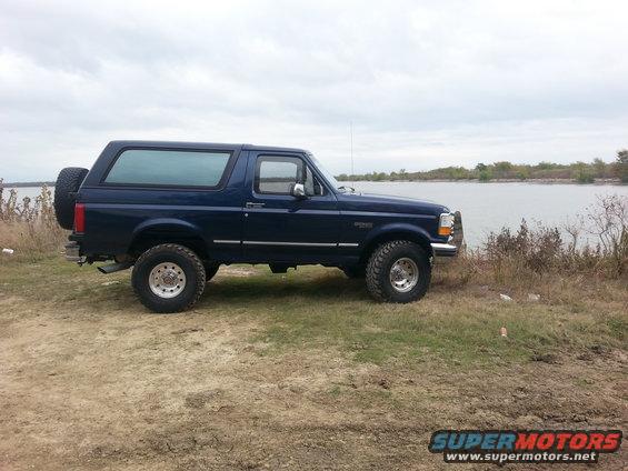 1995 Ford Bronco parked on dirt and grass next to a lake