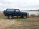 1995 Ford Bronco - Side view of a blue 1995 Ford Bronco parked near a lake under a cloudy sky.