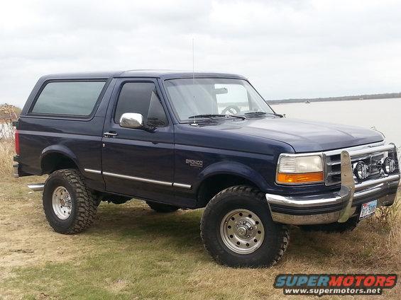 Dark blue 1995 Ford Bronco parked on grassy terrain near water, with a chrome brush guard and off-road tires
