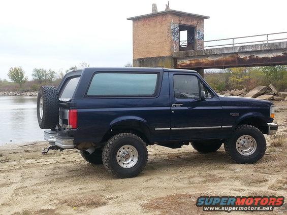 Dark blue 1995 Ford Bronco parked by water, spare tire on rear door