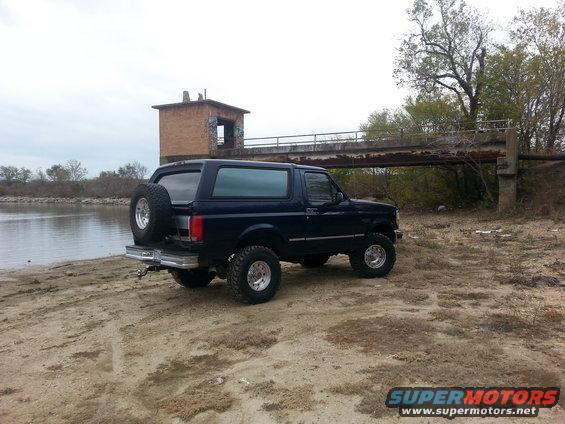 Dark blue Ford Bronco parked by a body of water near a bridge