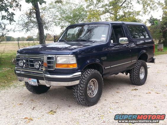 Dark blue Ford Bronco, 1992 model year, with chrome grille, aftermarket fog lights, and large off-road tires