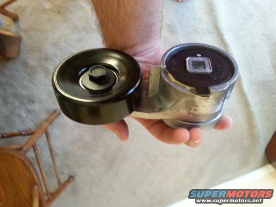 Belt tensioner assembly held in hand, showing two pulleys and metal bracket