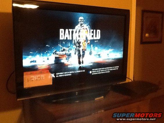 TV screen showing Battlefield title screen with a soldier and tank. Orange sticky note on the bottom left