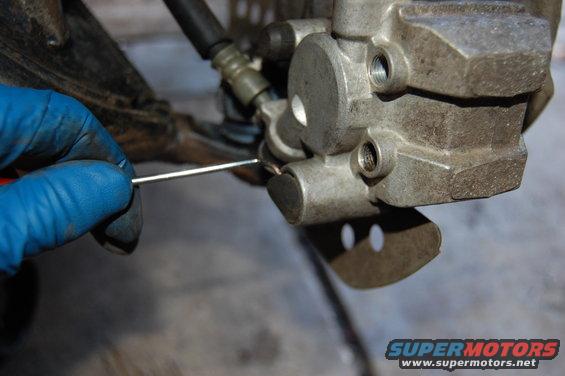 Close-up of ATV brake caliper being worked on with a tool and blue glove