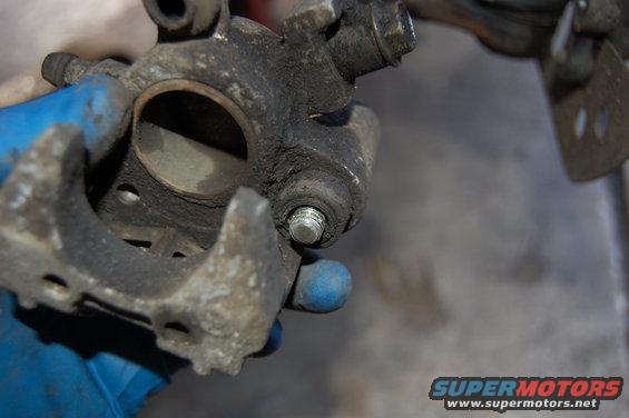 Close-up of a dirty brake caliper being held by a gloved hand