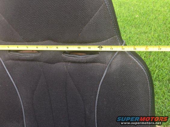 Measuring tape across a black car seat with two cutouts. Grass in background