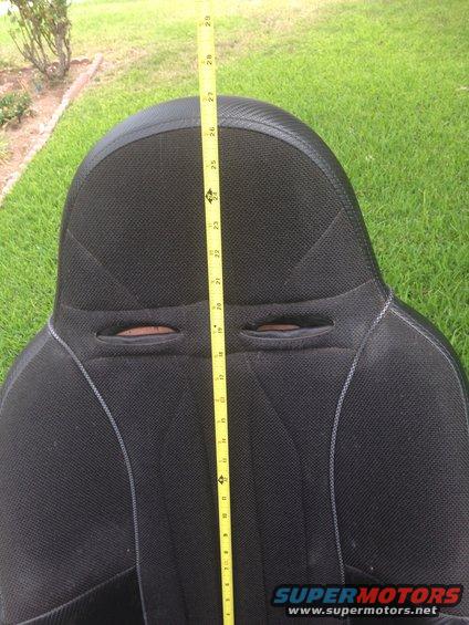 Black car seat with gray stitching and two harness cutouts, measured with a yellow tape measure