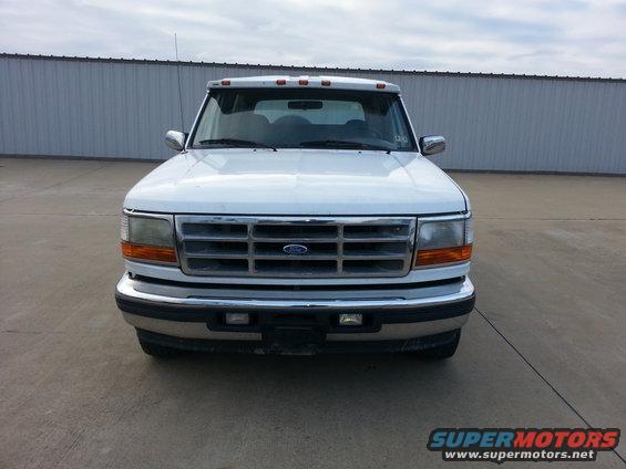 Front view of a white Ford F-Series truck with a chrome grille and a sun visor