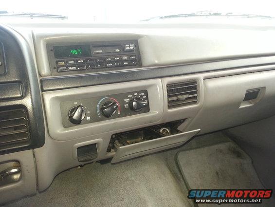 Gray dashboard interior with radio, climate controls, and open glove compartment. Clock shows 4:57