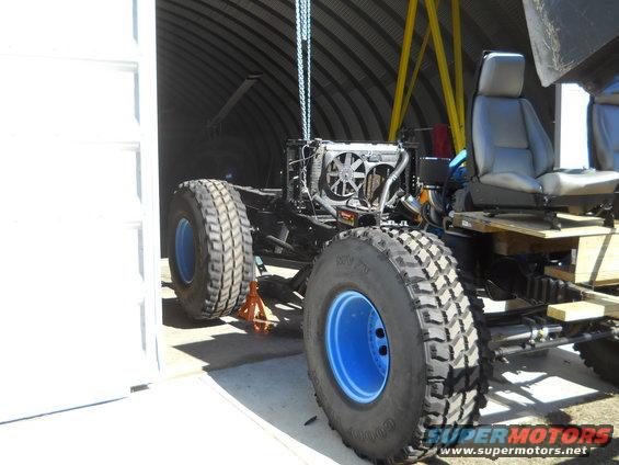 Off-road vehicle chassis with engine, radiator, and seats, raised on jack stands inside a Quonset hut