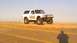 1996 Ford Bronco - A heavily modified white Ford Bronco sits on a sandy terrain under a clear sky.
