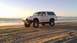 1996 Ford Bronco - A lifted Ford Bronco sits on a sandy beach near the ocean at sunset.