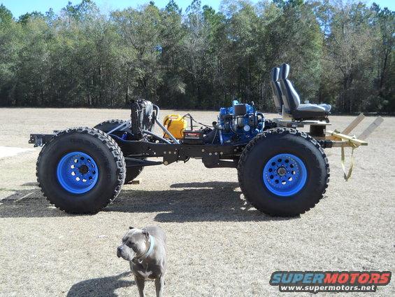 Custom off-road vehicle chassis with large tires, blue rims, and a blue engine, viewed from the side