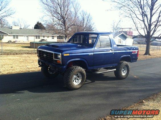 Blue lifted Ford Bronco parked on asphalt driveway in front of a house