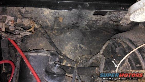 Engine bay with wiring, hoses, and battery components. Some dirt and grime are visible