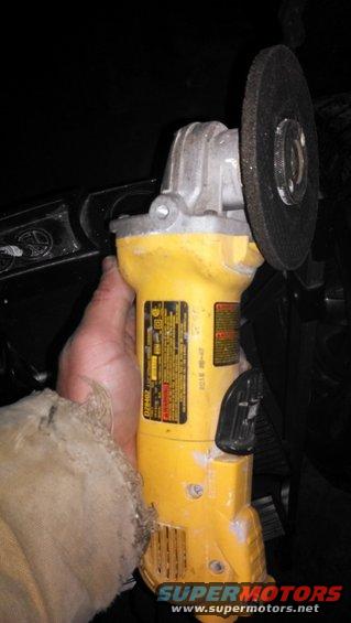 Yellow angle grinder with a cut-off wheel held by a hand wearing a tan sleeve