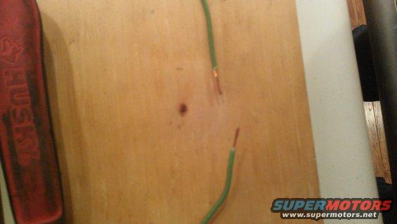 Exposed copper wire ends on a wooden surface, with a red tool handle on the left