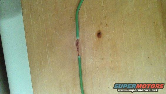 Damaged green wire with exposed copper strands on a wooden surface