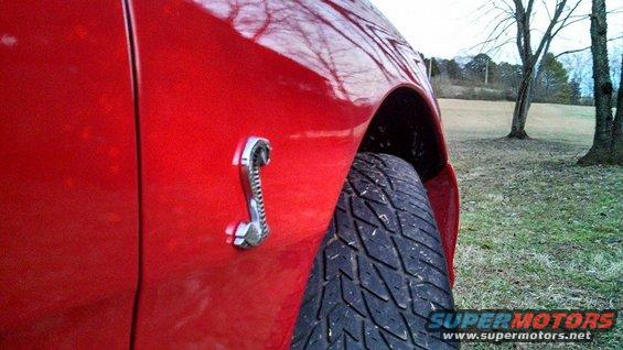 Close-up of a red car's side fender with a chrome cobra emblem and a tire visible