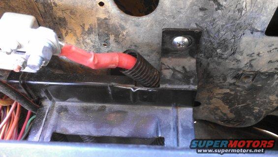 Close-up of a red wire with electrical tape and black corrugated tubing attached to a metal bracket