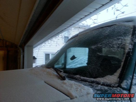 snow on windshield and hood of a vehicle parked in a garage