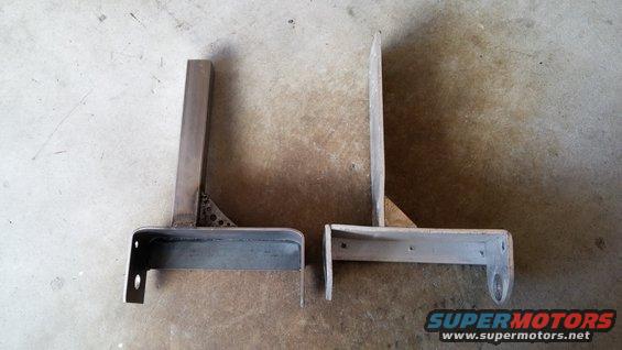 Two custom metal brackets, one with triangular bracing, sit on a concrete floor