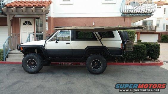 White and black SUV with awning, large tires, and spare tire carrier