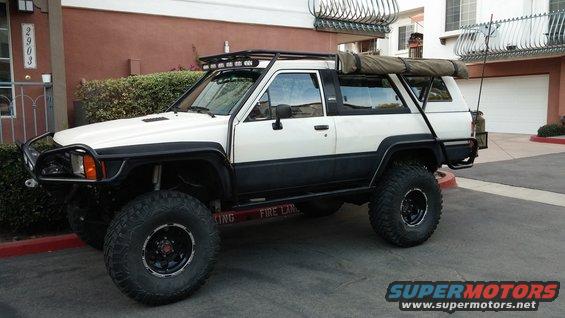 White and black Toyota 4Runner with off-road tires, roof rack, and awning