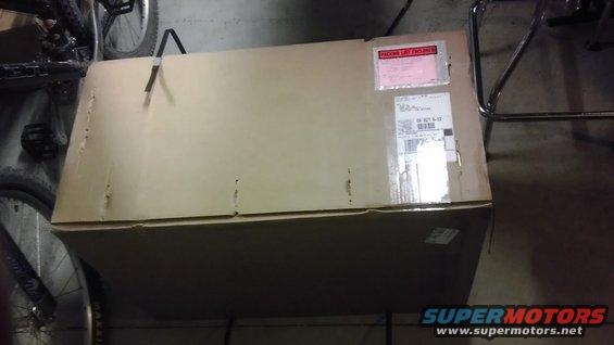 Cardboard box with shipping labels, next to a bicycle wheel and metal chair